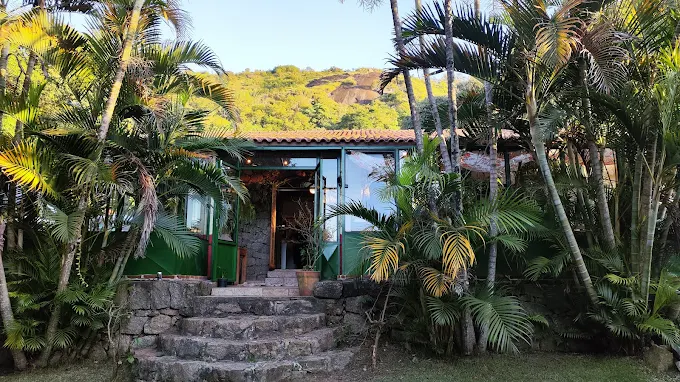 Fachada verde do Art & Fusão e a escadaria de pedra em meio ao jardim ao entardecer