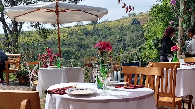 Mesa posta sob sombrinha no jardim do Art & Fusão, com o vale ao fundo