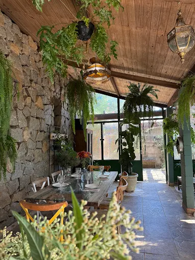 Salão de pedra e vidro com plantas suspensas e uma longa mesa preparada para o jantar
