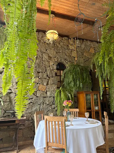 Cantinho de jantar com parede de pedra, samambaias e uma mesa com toalha branca